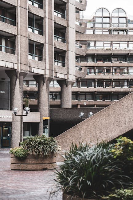 The image depicts an urban courtyard surrounded by a large, modern concrete residential building with multiple balconies and arched windows, characteristic of a high-rise structure. In the foreground,