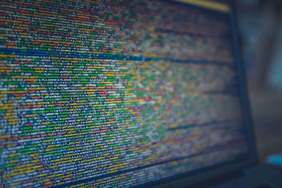 A detailed close-up of a computer screen displaying colorful lines of code in a programming interface. The screen shows various text elements in shades of green, yellow, blue, orange, and white, set a